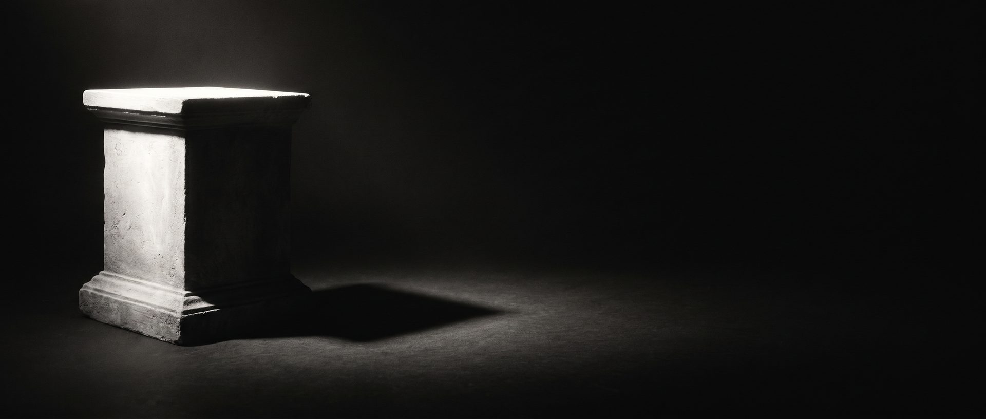 An empty stone pedestal set to one side, illuminated by a single spotlight that casts a sharp shadow across a dark floor.